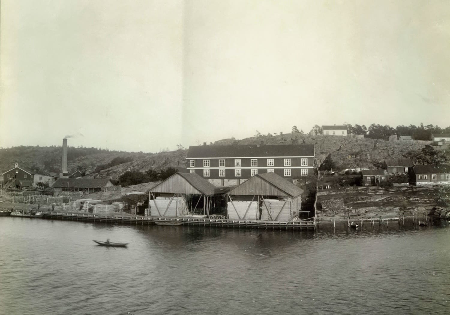 Foto tatt fra elven som viser Røds Bruk, Glombobrakka, plankelager og lasteplass fra 1895. Foto: Leverin / Digitalt museum.
